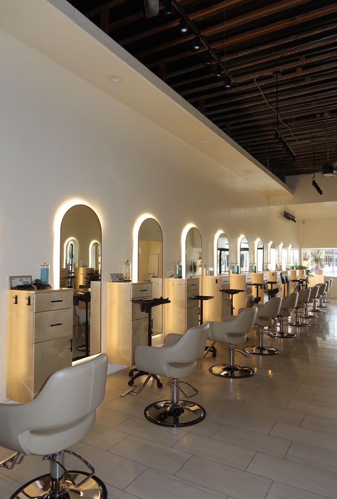 Bright Evolve Salon styling floor with a long row of backlit arched mirrors, blonde wood stations and cream chairs