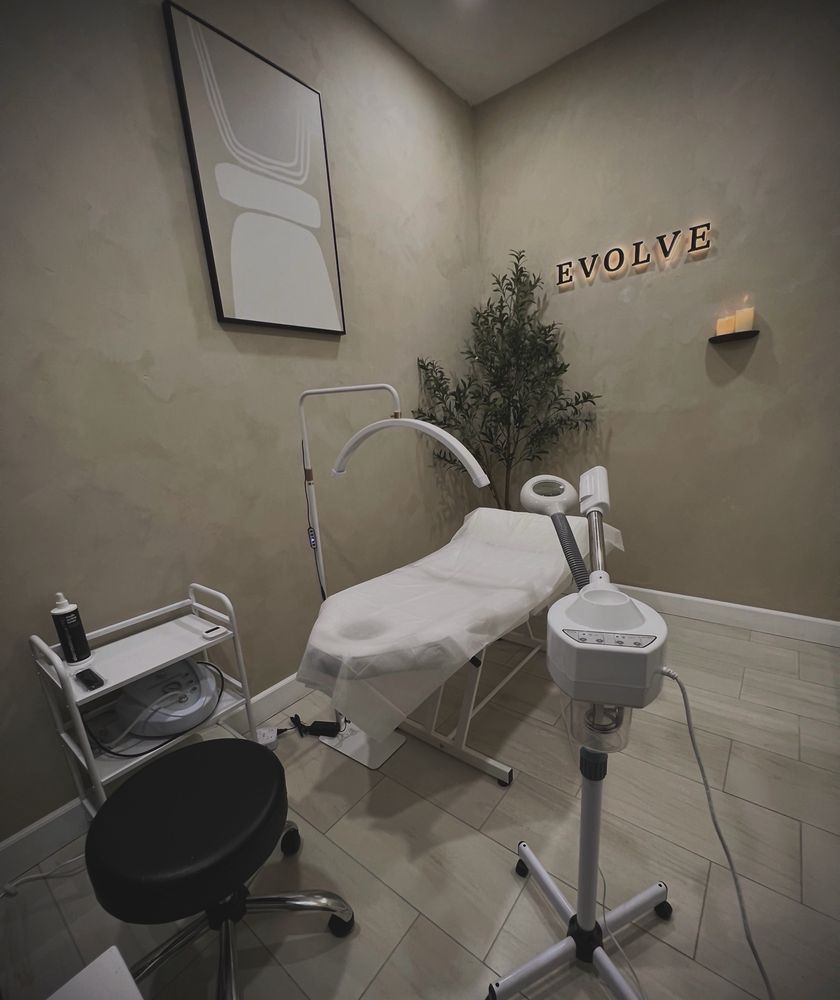 Private aesthetic treatment room at Evolve Salon with a treatment bed, magnifying lamp and the lit Evolve sign