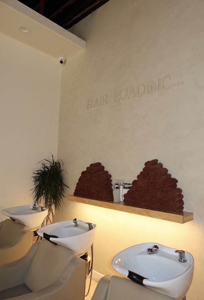 Evolve Salon backwash area with three shampoo stations, stacked espresso towels and a floating wood shelf
