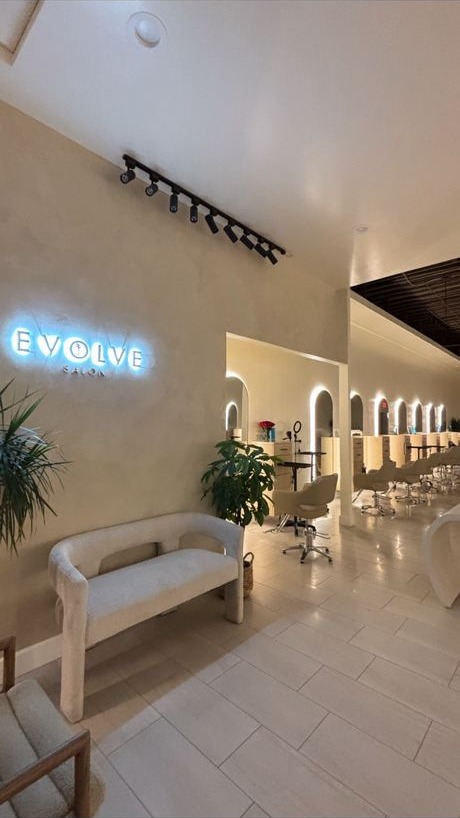 Evolve Salon entry and waiting bench beneath the glowing Evolve Salon sign, with the lit corridor of styling stations beyond