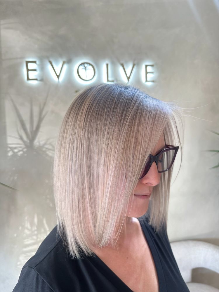 Shoulder-length ash blonde lob, straight and sleek, in front of the lit Evolve sign